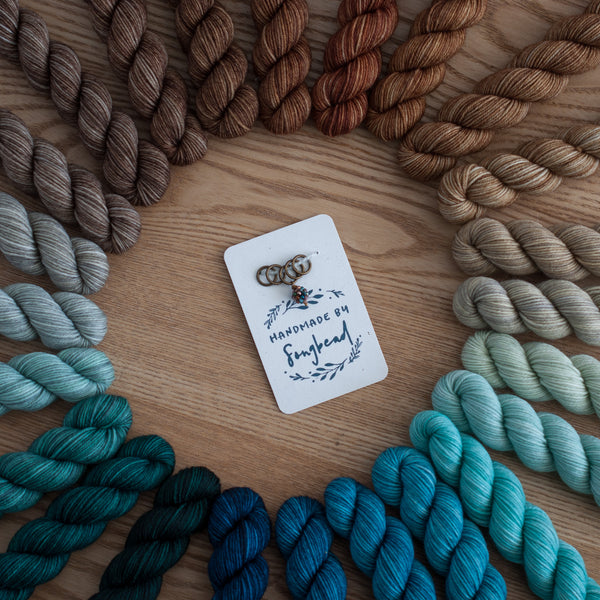 Colorful yarn skeins arranged around a card with 'Handmade by Songbead' on a wooden surface.