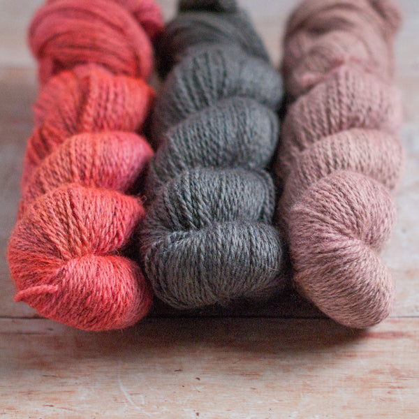 Three skeins of yarn in neon pink, grey, and light pink on a wooden surface