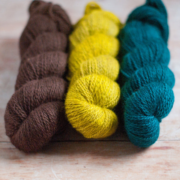 Three skeins of yarn in brown, yellow, and blue on a wooden surface