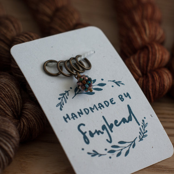 Handmade stitch markers on a card with yarn in the background
